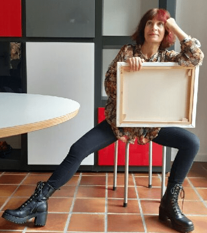 Portrait Photo de Malika Hachemi Milhorat, assise, le regard rêveur, une toile dans les mains