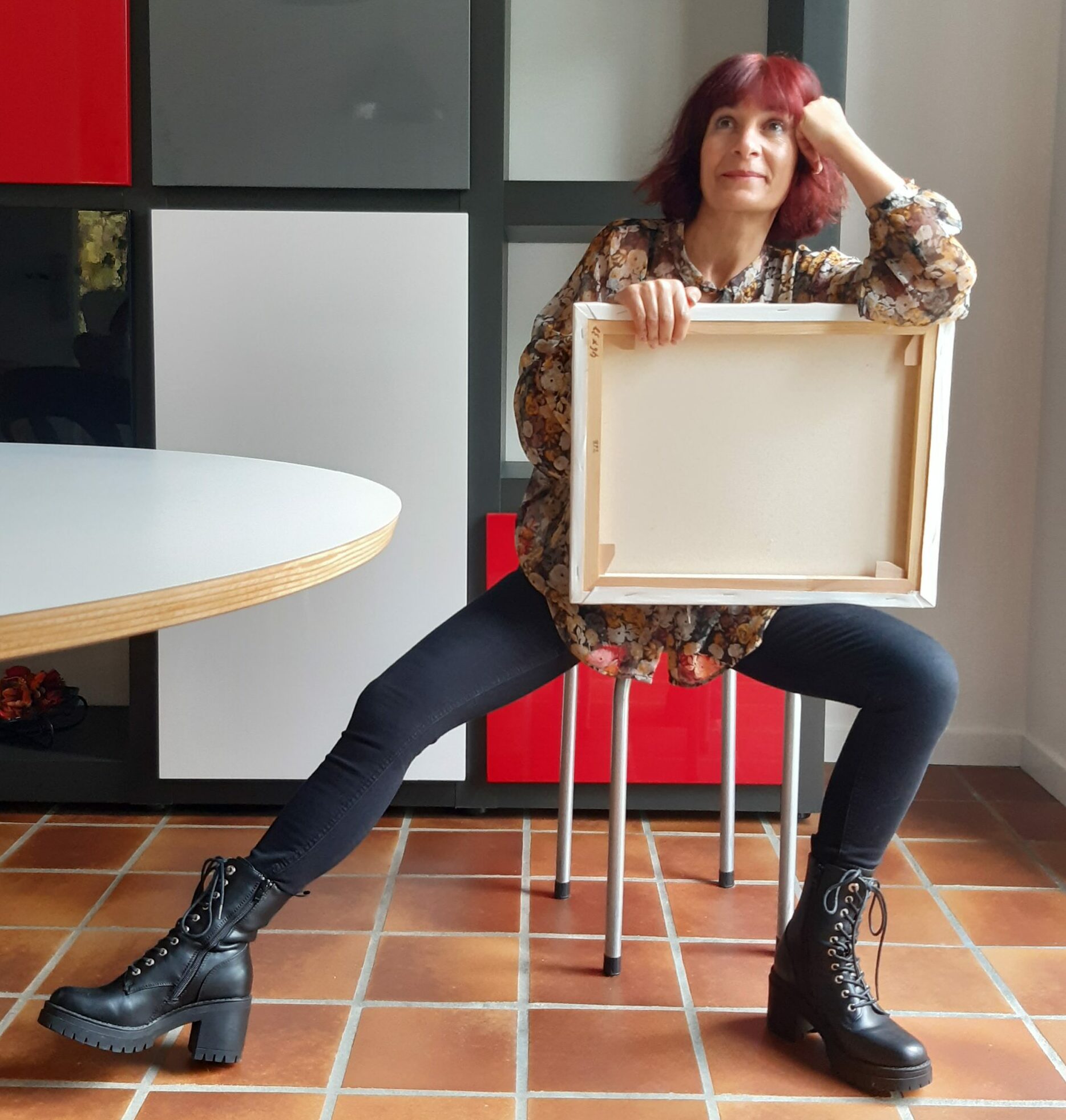 Portrait Photo de Malika Hachemi Milhorat, assise, le regard rêveur, une toile dans les mains